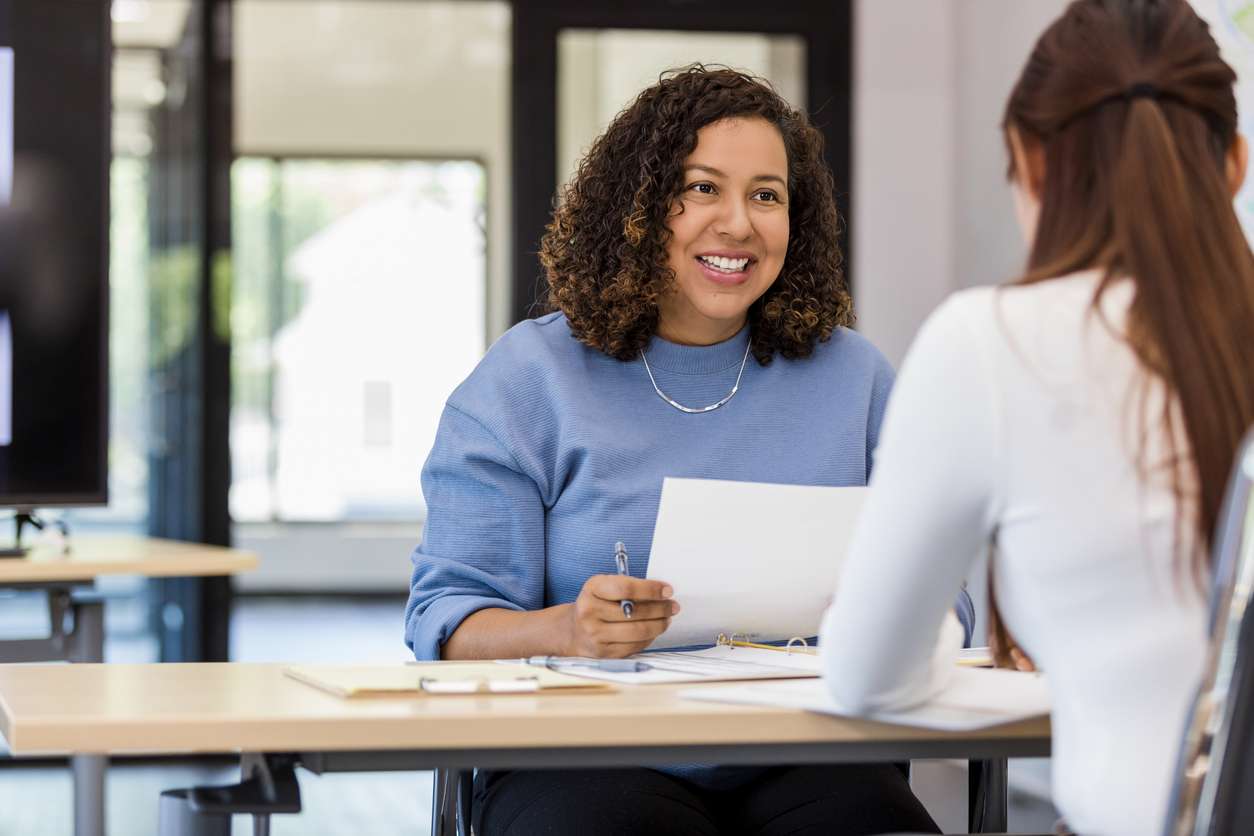 A female office manager is speaking to a female applicant inside the office. She is hiring employees in Canada.