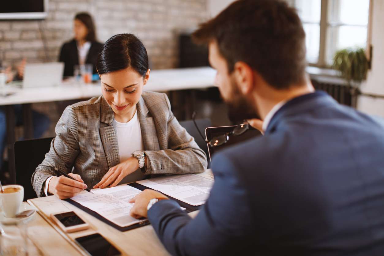 Creating a supportive work environment. • BrightR Understanding employee leaves - Female employee signing an employment contract in front of her male manager.