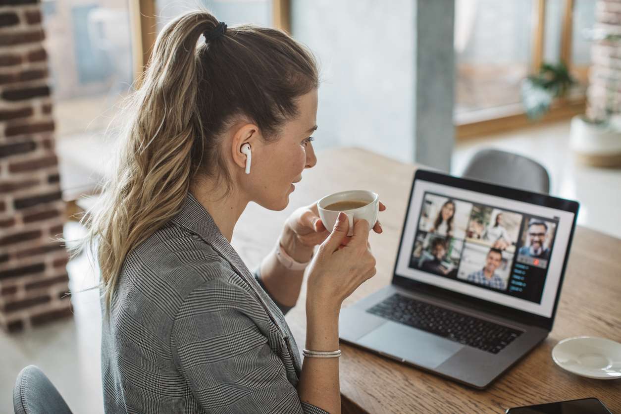 Conducting regular coffee meetings with your remote team. • BrightR Team building for remote workers - A businesswoman drinking coffee while having a virtual meeting with colleagues.