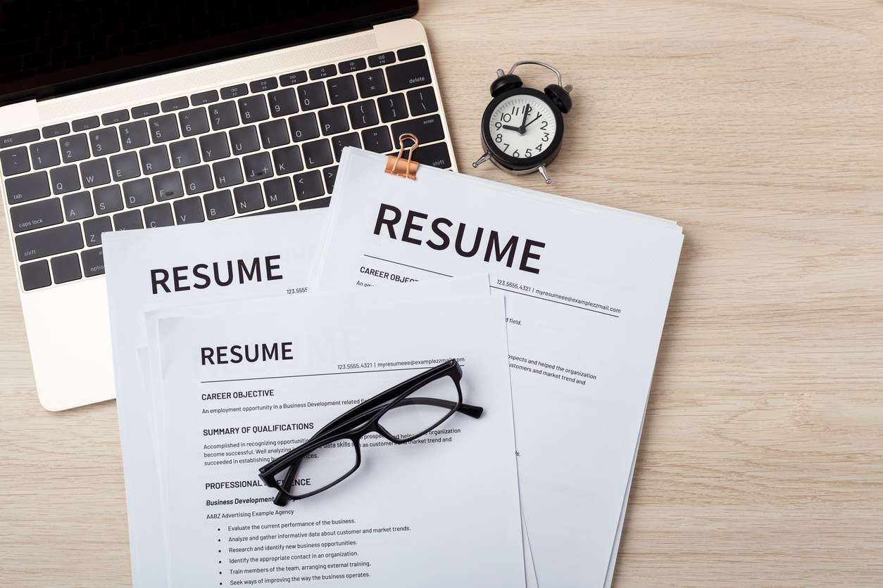 Comparing resumes for international hiring - Different employee resumes on a table with a laptop.