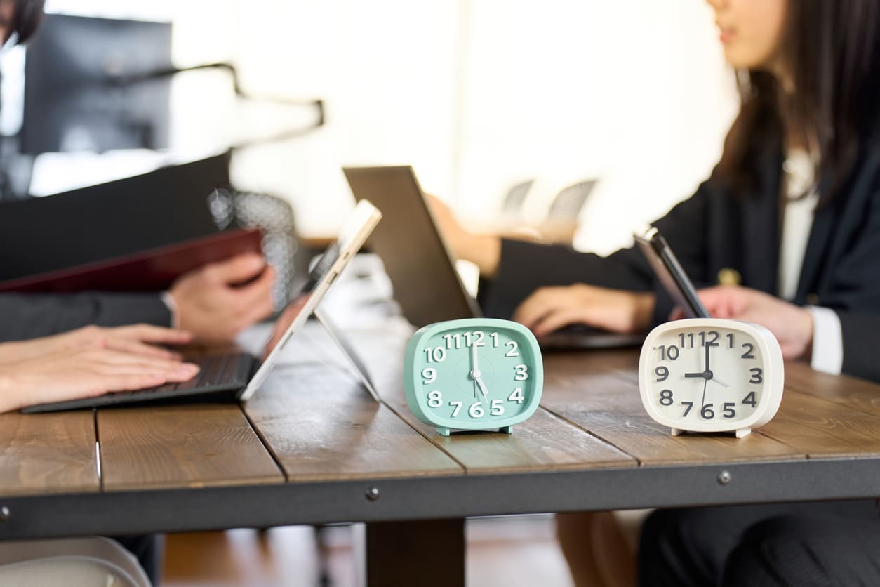 Time zone communication strategies - Two small clocks on a table with business owners working in the background.