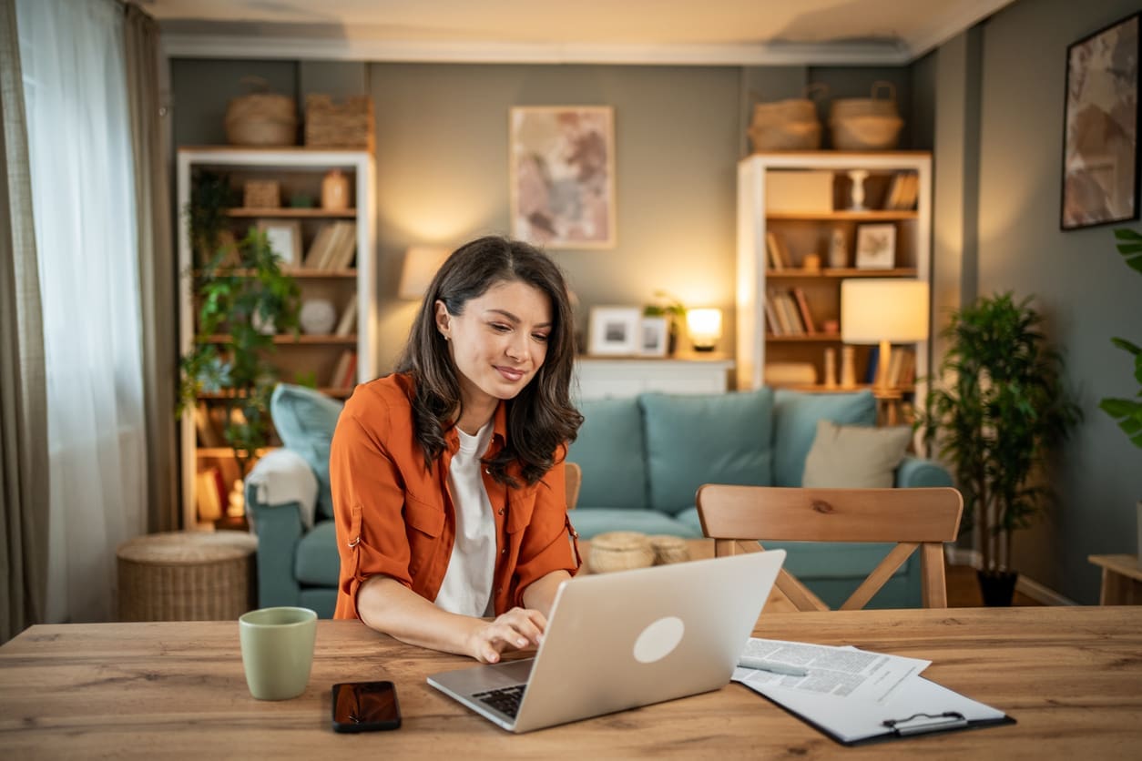 Developing time zone communication strategies - A woman at home using a laptop to accomplish work-related tasks.