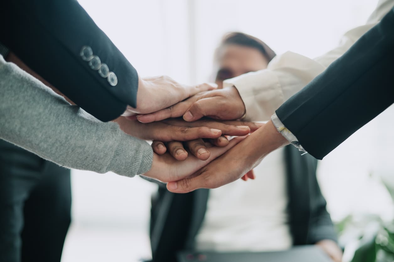 International team management - A diverse group of employees showing unity by putting their hands together on top of each other.
