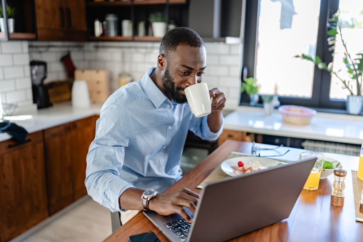 Work-from-home productivity - A man at home drinking coffee while checking his work emails.