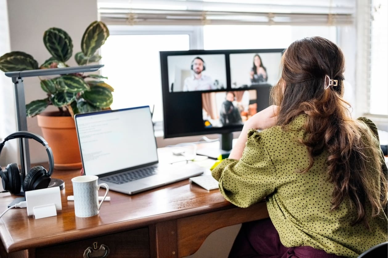 Global remote teams - A woman at home listening to her team's virtual presentation.