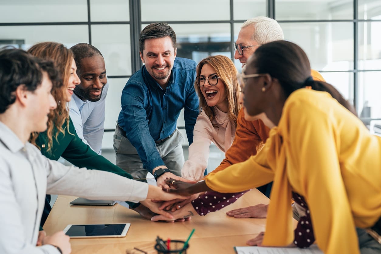 Employee engagement - A diverse group of happy employees stacking their hands together.