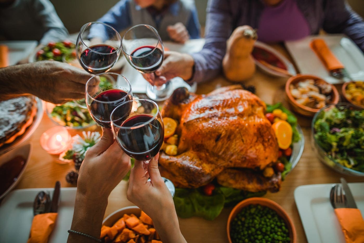 Group of people sitting around a table on Thanksgiving day toasting with glasses of red wine