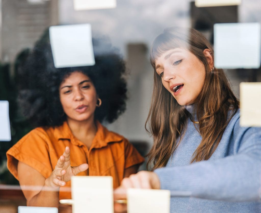 Hiring Local Staff: Real-Time Market Monitoring and Feedback • BrightR hiring local staff: females brainstorming in the office with post-its on w clear acrylic board.