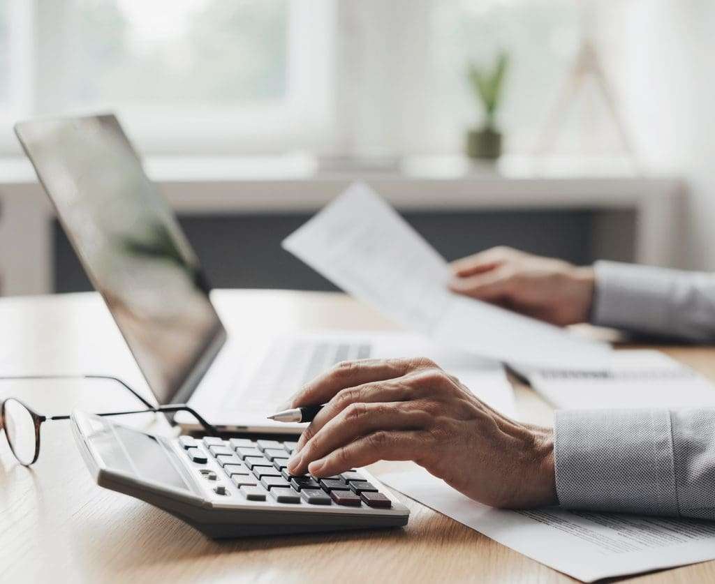 • BrightR Retention Processes Out-of-Country Staff: A cropped photo of a business person calculating using his calculator and laptop.