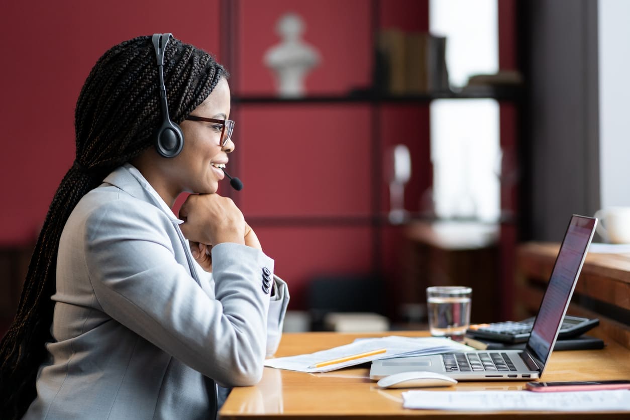 Remote staffing strategies - A female employee using a laptop and wearing a headset while working at home.