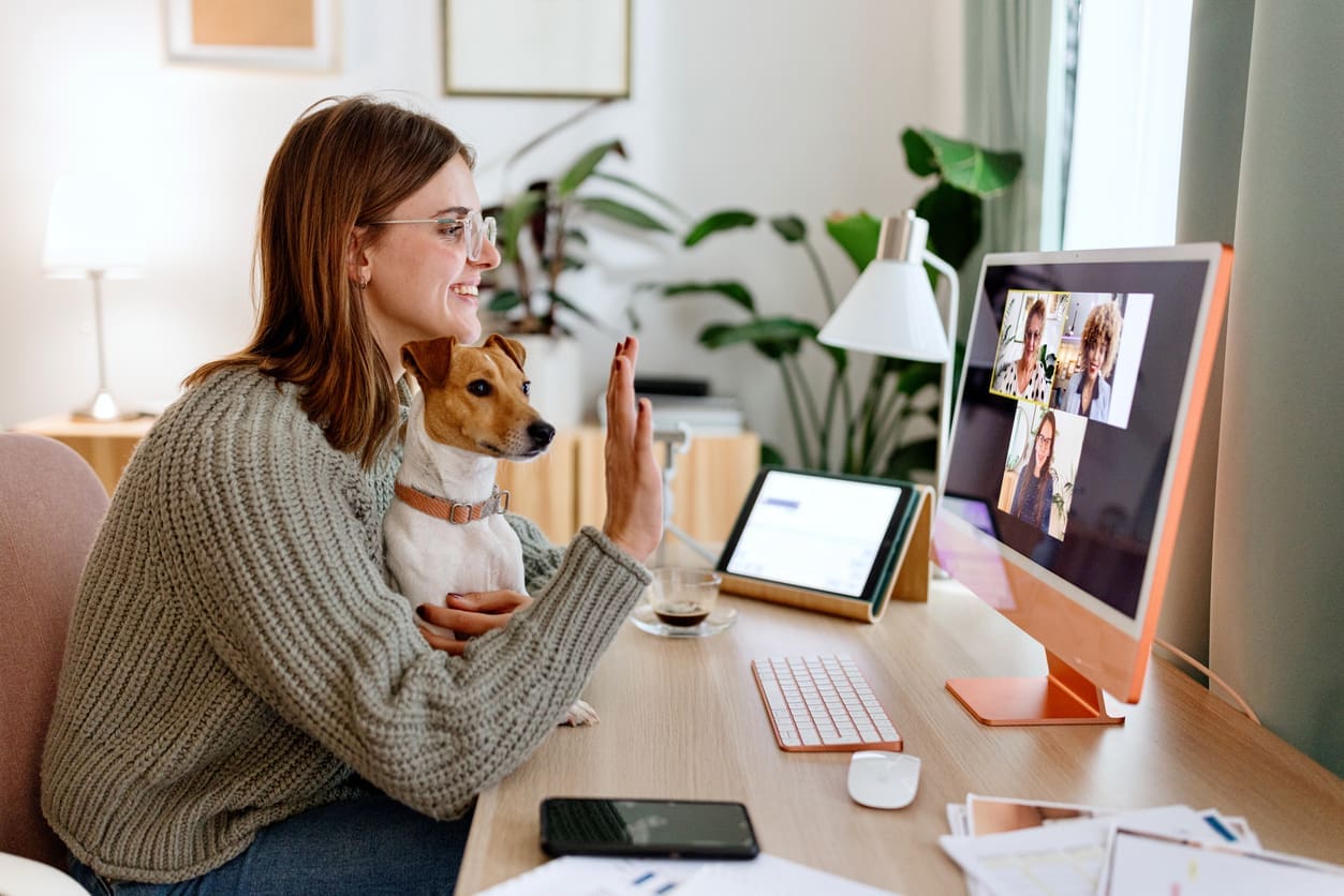 Fun company culture - A female remote worker holding her dog while having a meeting with her colleagues.