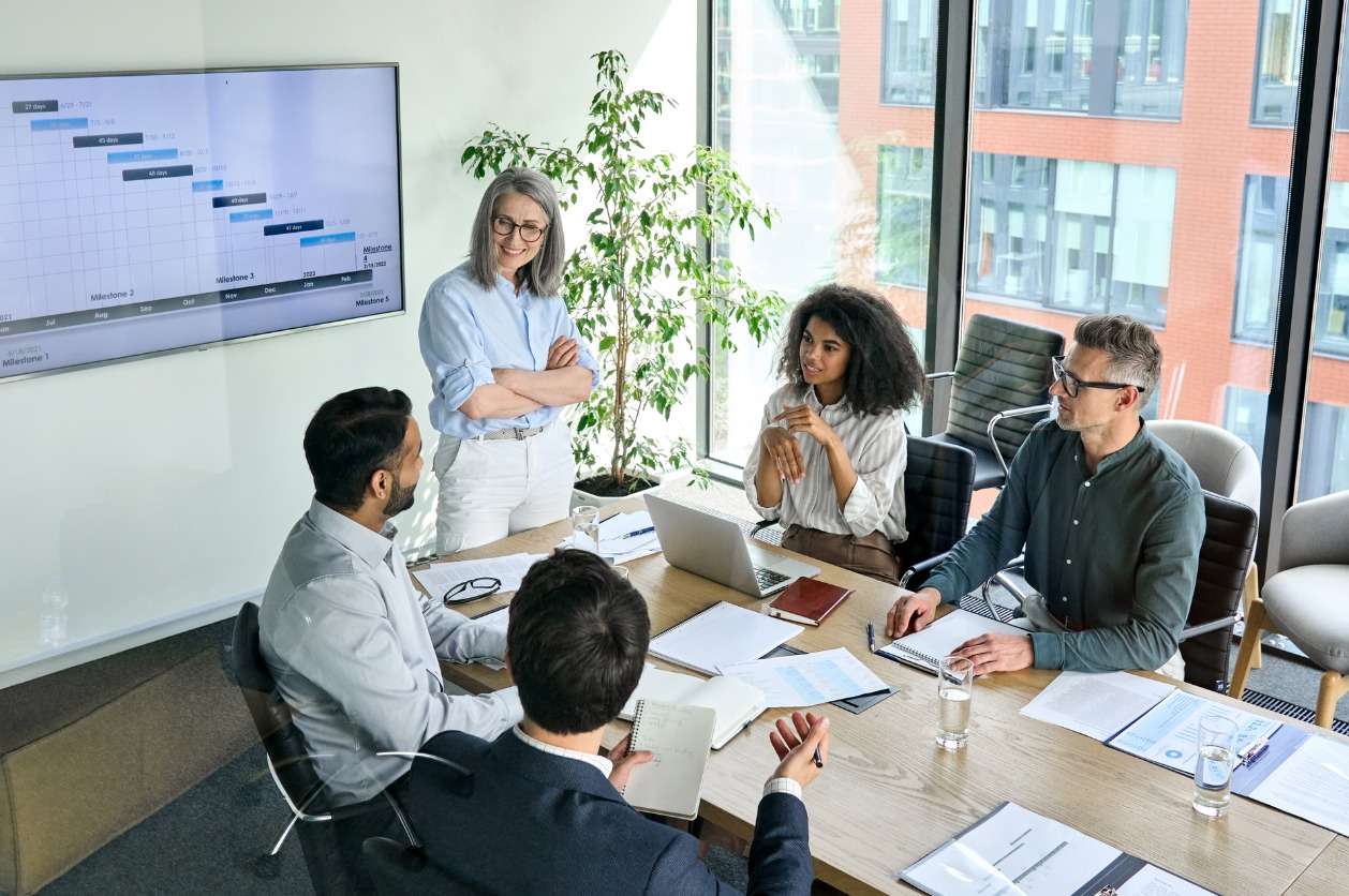 Communicating goals with team members and stakeholders. • BrightR Global workforce management strategies - A businesswoman having a meeting with her employees in a conference room.