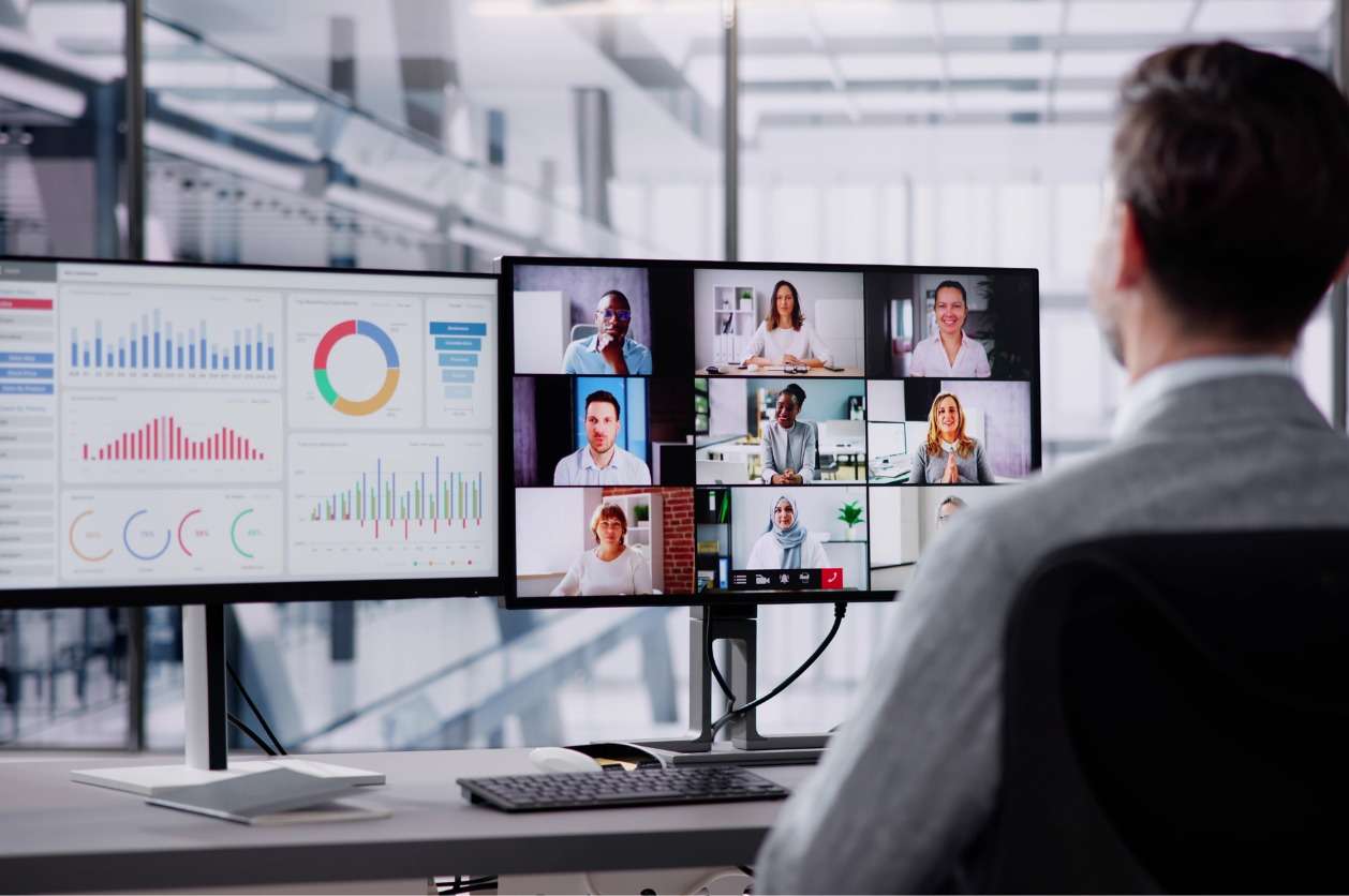 Tracking performance objectives and KPIs - A businessman having a virtual meeting with his employees while looking at a computer screen showing different graphs.