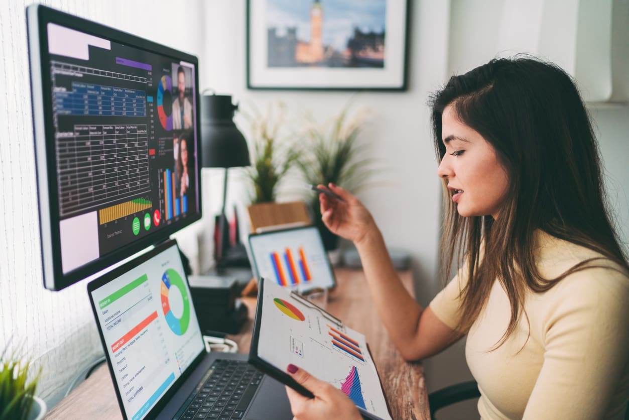 Remote team collaboration - A woman having a virtual meeting with her colleagues using a computer and other electronic devices.