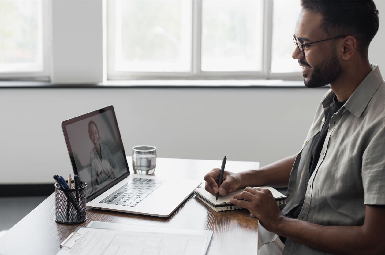 Remote onboarding buddy - A male employee having a virtual meeting with his mentor using a laptop.
